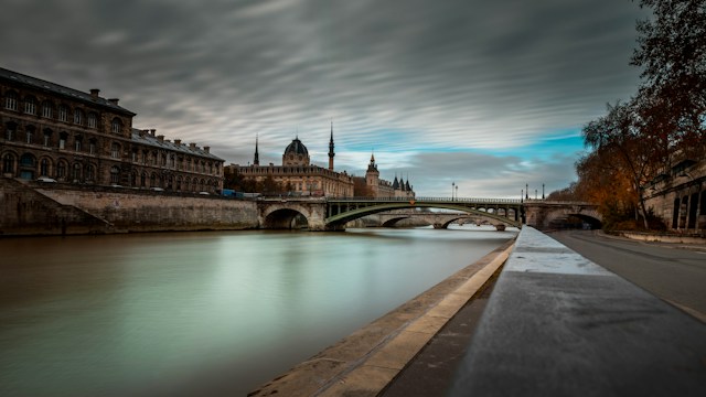 France in Contrast: Parisian Elegance and Bordeaux’s Wine Heritage River flowing past buildings and bridge under cloudy sky, Paris, La Seine